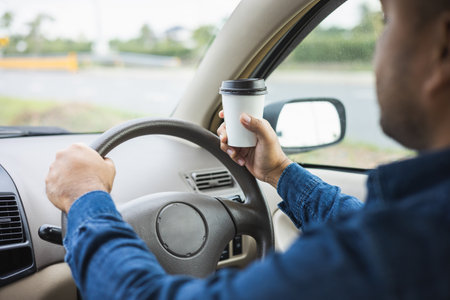 Young man drinking a cup of hot coffee while driving car to travel. Hands holding steering wheel.