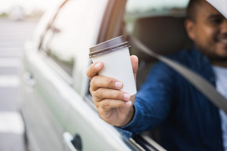 Young man drinking a cup of hot coffee while driving car to travel. Hands holding steering wheel.
