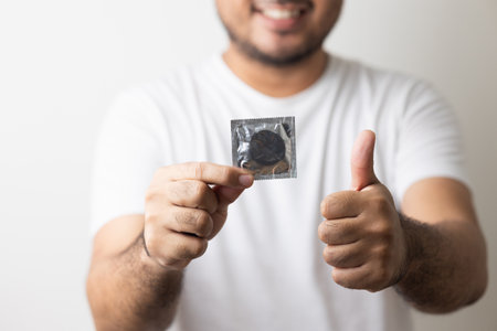 The young man showing the condom into camera. Campaign for safe sex and contraception. Close up male hand holding the condom.の写真素材