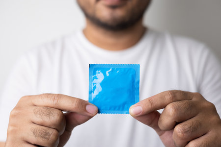 The young man showing the condom into camera. Campaign for safe sex and contraception. Close up male hand holding the condom.の写真素材