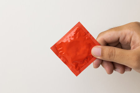 The young man showing the condom into camera. Campaign for safe sex and contraception. Close up male hand holding the condom.の写真素材