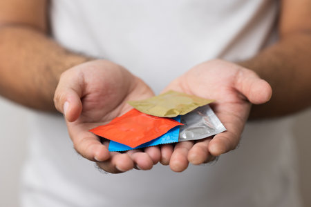 The young man showing a lot of colorful condom into camera. Campaign for safe sex and contraception. Close up male hand holding the condom.の写真素材