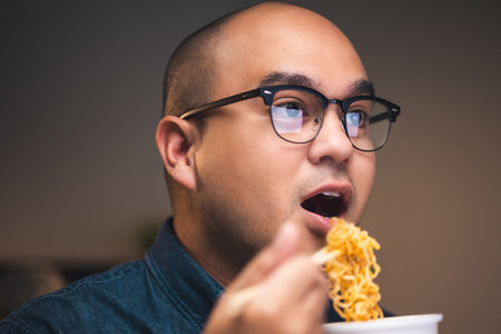 Young asian business freelancer working at late night. He very hungry and eating hot instant noodle and work with computer in the dark office at night.の写真素材