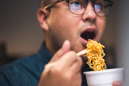 Young asian business freelancer working at late night. He very hungry and eating hot instant noodle and work with computer in the dark office at night.の写真素材