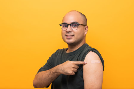 Vaccinated asian man showing arm after coronavirus Vaccination isolated yellow Background. Indian...