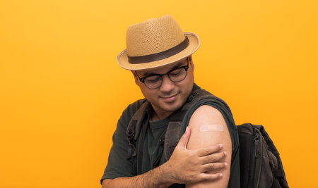 Vaccinated. Traveler asian man showing arm after coronavirus Vaccination isolated yellow Background....
