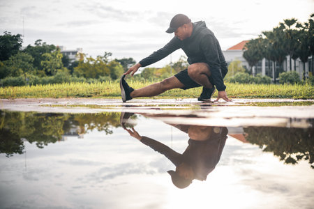 Young asian man wearing sportswear running outdoor. Portraits of Indian man stretching leg before running on the road. Training athlete work out at outdoor concept.の写真素材