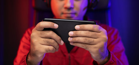 Playing video game on smartphone. Young asian handsome man sitting on chair holding cellphone in...