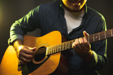Close up hands young man playing acoustic guitar on stage live in concert. With neon light. Young man practicing music and solo guitar on the show.の写真素材