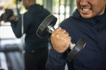 Young Fitness man with dumbbell in gym. Guy weight training wearing sportswear. Asian man exercise...