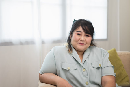 Happy women's plus sitting on sofa in living room. Body positive plus size female lives happily and is proud of herself.の写真素材