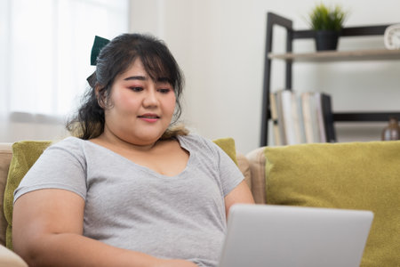 Body positive plus size female using laptop to video conference and working quarantine stay at home. Happy women's plus size video call in living room.の写真素材