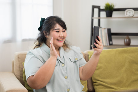 Body positive plus size female holding mobile phone taking selfie photo using smartphone camera. Happy woman plus size video call in living room.の写真素材
