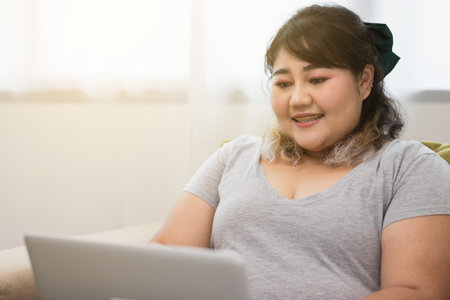 Body positive plus size female using laptop to video conference and working quarantine stay at home. Happy women's plus size video call in living room.の写真素材