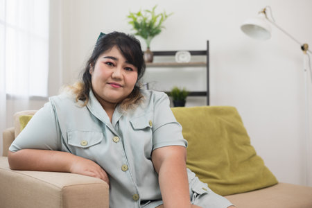 Happy women's plus sitting on sofa in living room. Body positive plus size female lives happily and is proud of herself.の写真素材
