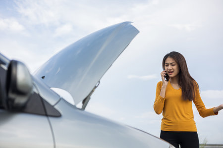 Young asian woman has broken down car on the road she feeling serious and stressed. Look for someone help. Using smartphone Call Emergency assistance or insurance service.の写真素材