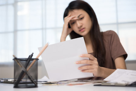 A young Asian woman is stressed because she looks at many expense bills and she has no money to pay them. Hand on head feeling very serious depressed.の写真素材