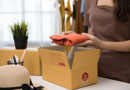 Woman business owner at fashion store packing clothing in the paper bag and delivery to customer....