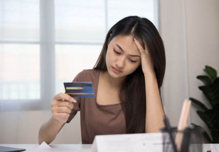 A young Asian woman is stressed because she looks at many expense bills and she has no money to pay them. Not enough money on credit card to payの写真素材