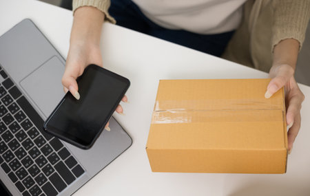 Close up business woman hand sending product to customer using smartphone scan qr code on the box....