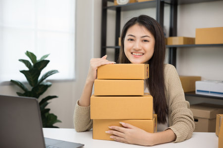 Young beautiful asian entrepreneur stacking the parcel cardboard and hugging product and smile to...