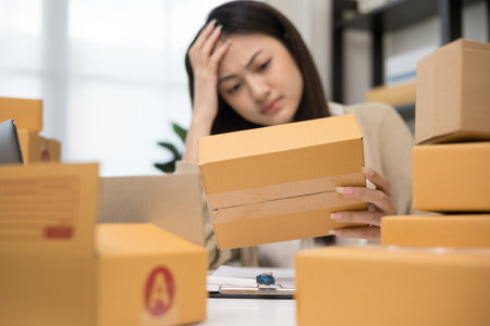 Busy and stressed asian entrepreneur woman checking product on stock working with laptop. Business woman working SME online at home. Small business owner start up freelance concept.の写真素材