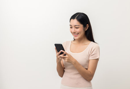 Excited Beautiful young asian woman using smartphone mobile standing on isolated white background. Playing game on smartphone winning victory moment. Very happy enjoy and fun relax timeの写真素材