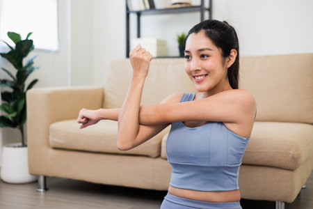 Attractive asian young fitness woman stretching arms warming up before workout at home. Beautiful smiling Female wearing sportswear exercise training yoga in living room.の写真素材