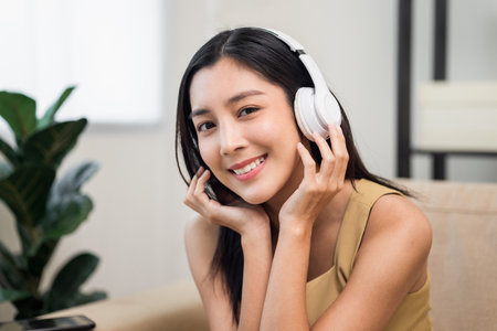 Relaxing time with music. Beautiful young asian woman sitting in the house choose music and take a rest and listening song with wireless headphone. Lifestyle in living room at house in the morning.の写真素材