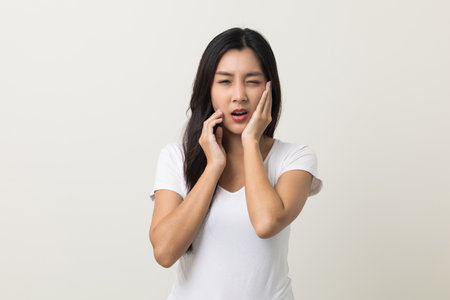 Asian woman puts her hand on her mouth and feels toothache because of tooth decay. Problems with teeth bad breath. Asian woman around 25 standing on isolated backgroundの写真素材