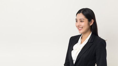 Young asian business woman smiling standing looking at blank space on isolated white background. Female around 25 in suit portrait shot in studio.の写真素材
