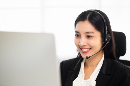 Call centre female operator. Smiling asian business woman receptionist wearing headphone video conference calling talk by webcam in online chat customer support service.の写真素材