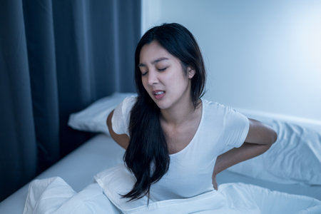 Waking up with a backache. Woman can't fall asleep moving restless on bed. Young woman having sleep troubles trying can not sleep.の写真素材