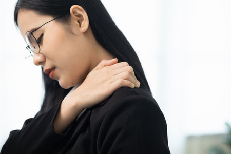 Office syndrome concept, Asian business woman works at computer, she experiences pain in neck and touches his neck with one hands, turns his head in attempt to relieve pain.の写真素材