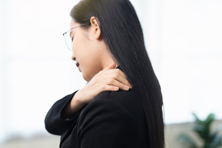 Office syndrome concept, Asian business woman works at computer, she experiences pain in neck and touches his neck with one hands, turns his head in attempt to relieve pain.の写真素材