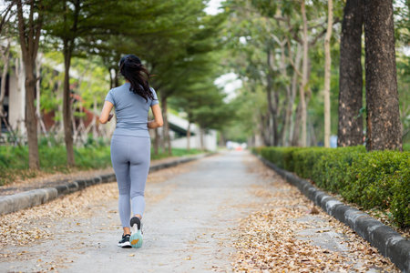 Happy slim woman wearing sportswear jogging in the city at sunrise. Young beautiful asian female in...
