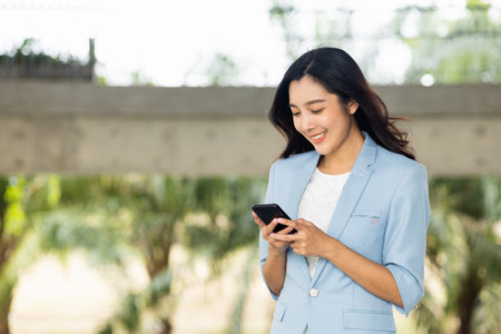 Beautiful business woman using mobile phone to play social media in the buildings at downtown. Smart female using cell phone chatting for business communication. Smartphone concept.の写真素材