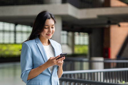 Beautiful business woman using mobile phone to play social media in the buildings at downtown. Smart female using cell phone chatting for business communication. Smartphone concept.の写真素材