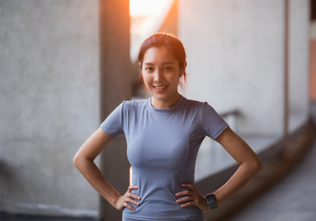 Portrait young beautiful asian woman wearing sportswear standing pose smiling in the city at sunrise. Cheerfully sporty female workout and exercise in the morning.の写真素材