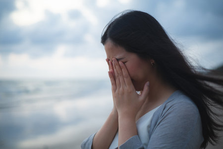 A sad and stressed Asian woman stands alone on the beach in the evening. Dramatic atmosphere. disappointment in life. She stood crying aloneの写真素材