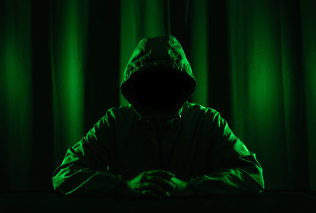 Hackers wear hoods to cover their faces. Hacking to steal important information. Use a computer to release malware viruses Ransom and harass organizations. He sitting in the dark room with neon lightの写真素材