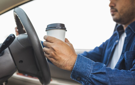 Young man drinking a cup of hot coffee while driving car to travel. Hands holding steering wheel.