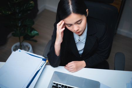 Stressed asian business woman working late at night in the office hands on head feeling headache....