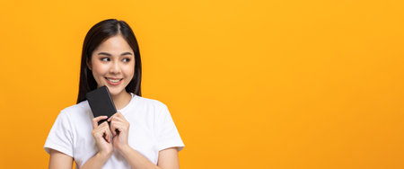 Pretty young asian woman using smartphone standing on isolated yellow background feeling happy....