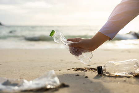 Close up woman hand pick up the plastic bottle on the beach. Female Volunteer clean the trash on the beach make the sea beautiful. World environment day concept.の写真素材