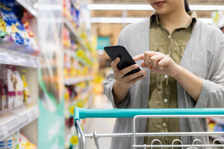 Close up hands woman checking shopping list on her smartphone in supermarket with trolley cart. Female using smartphone and application check product informationÂ in supply modern trade hall.の写真素材