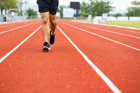 Close up legs Young chinese man wearing sportswear running on track at sport stadium. Fit man jogging outdoor cross the finish line. Exercise in the morning. Healthy and active lifestyle concept.の写真素材