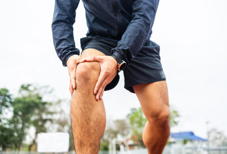 Young man runner has sore knee because he ran too long. Male Exercising until the injury. Overtrained. Young sport man accident running on trackの写真素材