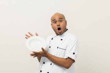 Wow excited menu. Young handsome asian man chef in uniform holding empty plate delicious dish menu good taste on isolated. Cooking indian man Occupation chef People in kitchen restaurant and hotel.の写真素材