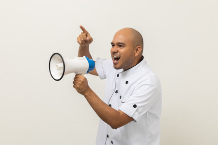 Shout out loud order excited face with mega phone Young handsome asian man boss chef in uniform command order the staff for menu on isolated. Cooking indian man chef in kitchen restaurant and hotel.の写真素材